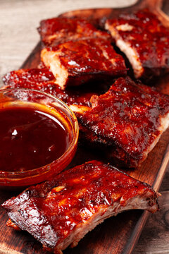 BBQ ribs with sauce served on a wooden board in a kitchen setting