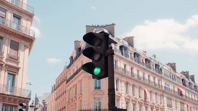 Close up view of a traffic light switching from red to green light on a sunny day in Paris. Haussmann style residential buildings and blue sky in the background. High quality 4K video.