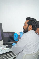 A research team talk through data in a team meeting before monitors showing scientific data while...