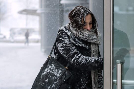 Woman in warm coat and scarf walking to work in snowy winter city street. Girl commuting in cold weather during snowfall. Bad weather, freezing temperature and urban lifestyle concept.