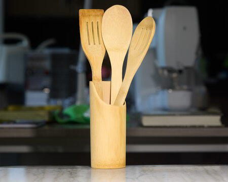 Assorted wooden kitchen utensils &ndash; spatula, spoon, and slotted turner &ndash; neatly arranged in a bamboo holder on a clean kitchen counter. Essential tools for healthy cooking and home preparation.