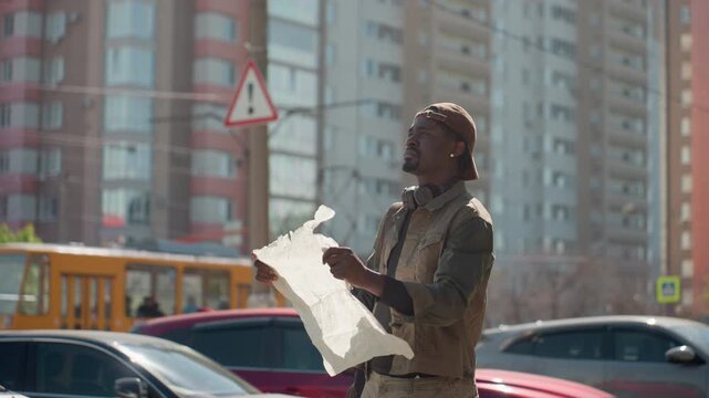 Close up of man examining large white paper map in urban street setting with cars and tall buildings. Man holds crumpled document appearing to read or orient himself using it. Bright