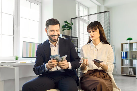 Employees in office, man and woman compare salary. He counts money and smiles while she holds fewer cash bills, revealing pay gap and inequality in compensation. Symbol of unfair salary gap.