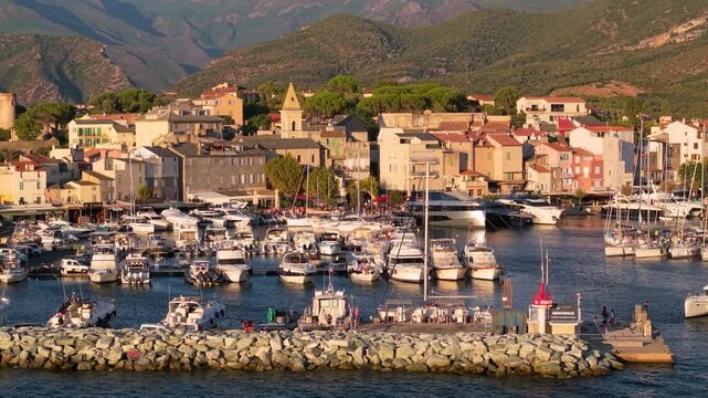 Saint Florent Citadel and marina aerial 70mm drone view with white catamaran in Corsica. Telephoto panning shot of Genoese fortress town port golden hour 4K