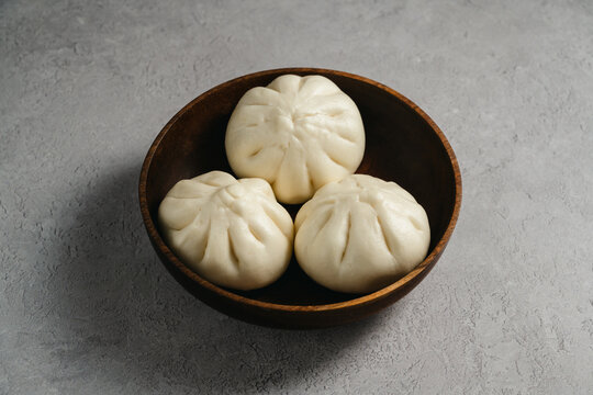 Traditional steamed bao buns on a dark wooden bowl