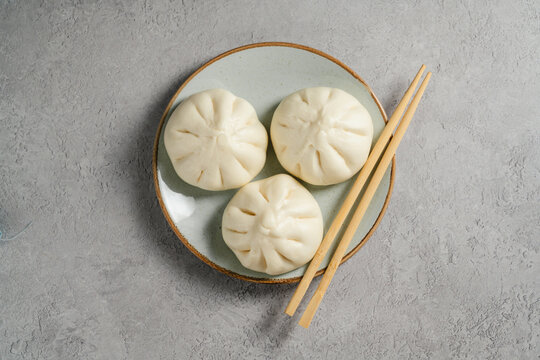 Steamed bao buns arranged on a ceramic plate with chopsticks