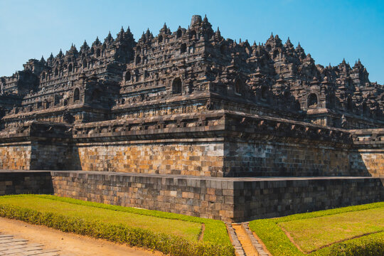 Monumental Stepped Stone Terraces of Borobudur Temple with Green Lawns Under Clear Blue Sky in Central Java Indonesia