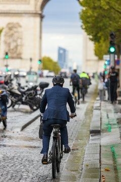 Businessman in a suit rides a bicycle toward the Arc de Triomphe on a wet Paris street, symbolizing sustainable urban transportation and commuting