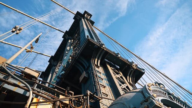 Steel tower and cables of Manhattan Bridge from below. A wide low angle composition emphasizes rivets, trusses and diagonal suspension lines.
