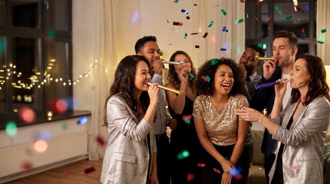 Friends celebrating at an elegant indoor party, laughing and blowing colorful noisemakers beneath falling confetti, with warm string lights, festive attire, and generous copy space along left.