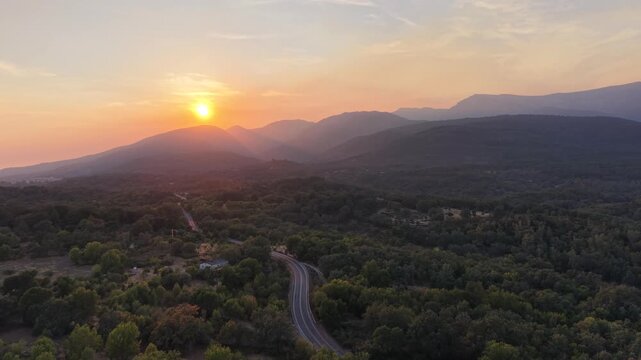 Aerial view of the landscape near Villanueva de la Vera at sunset, with a winding road through the forest and mountains under a golden sky in Villanueva de la Vera, Extremadura, Spain.