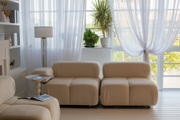 Modern beige sofa set in a bright living room interior with sheer curtains, a floor lamp, and houseplants near the window. High quality photo © Татьяна Швец