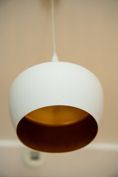 Modern pendant lamp with white shade and copper interior hanging against a beige wall, concept of home interior lighting design