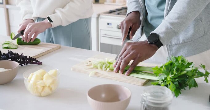 Couple placing boards slicing cucumber and celery with chef knives at kitchen island