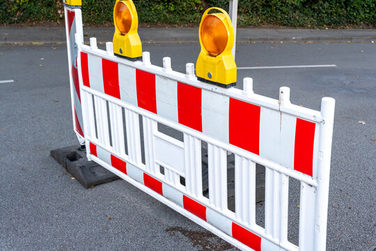 Red and white traffic barrier with warning lights placed on a road surface