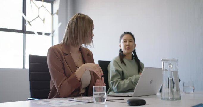 Team discussing at table, left female gesturing to prompt right nonbinary typing laptop to respond