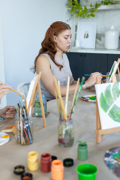Two women painting on tabletop easels at home studio with brushes, paint pots, cucumber water