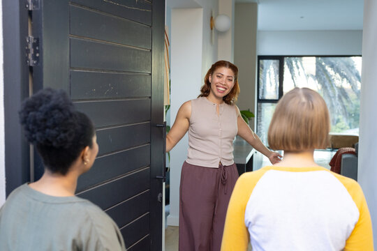 African American woman greeting women at home entry, holding dark paneled door, palm trees visible