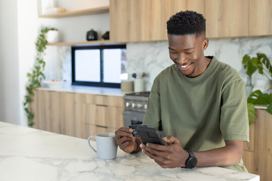 Man sitting at marble kitchen island using handheld device, holding card and ceramic mug