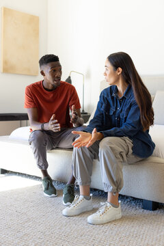 Diverse couple sitting on light-colored sofa in bright living room, man gesturing, woman listening