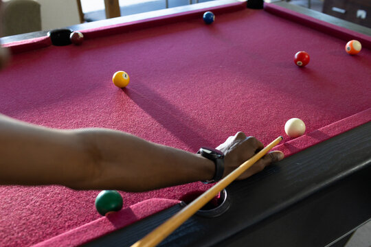 African man holding cue, aiming cue ball on pool table in lounge, shirt, watch, copy space