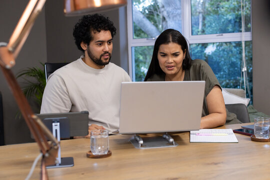 African American couple leaning forward and frowning at laptop on metal stand at home