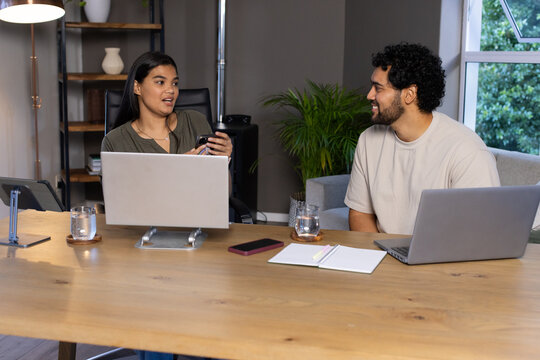 African American coworkers discussing ideas at office desk with two laptops and smartphone