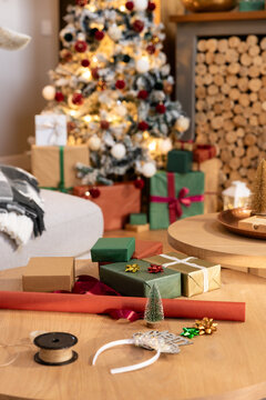 Wrapped gifts and wrapping supplies resting on round wooden coffee table in cozy living room