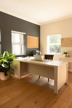 White rectangular desk is sitting centered on wood floor with open laptop and chair tucked behind