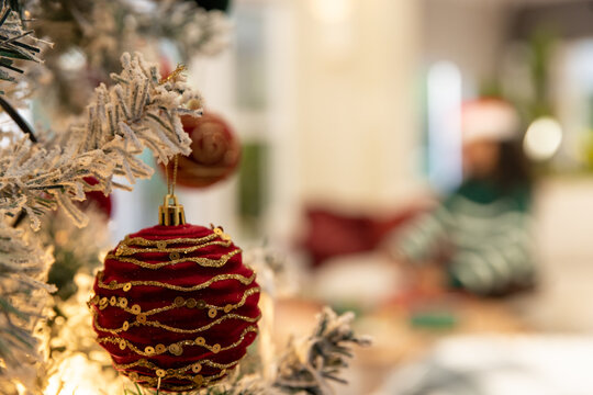 Red holiday bauble glistening on frosted evergreen branch with warm string lights in living room