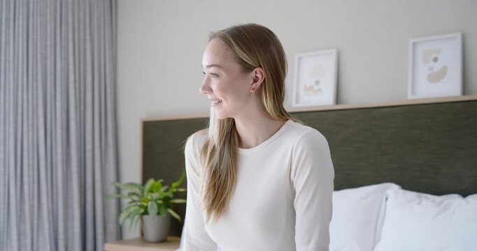Adult woman sitting on bed turning to camera while camera moving in, leaning smiling with duvet