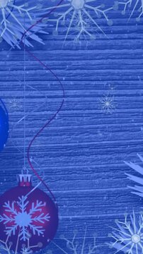 Animation of snowflakes icons falling over hanging bauble decorations against wooden surface