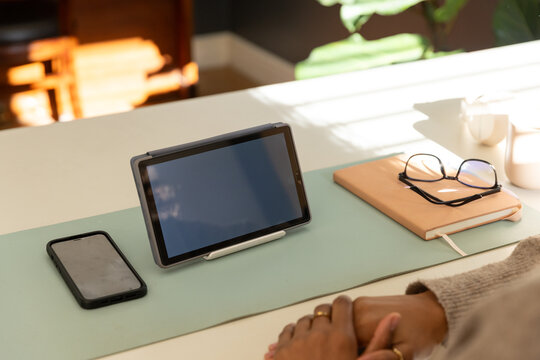 African American woman sitting at home desk in beige knit sleeve with gold rings near tablet