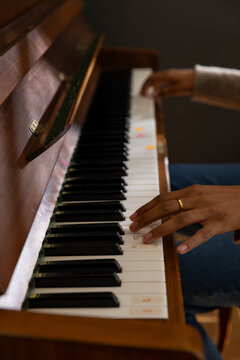 African American woman playing upright piano keyboard at home with colored stickers, wearing jeans