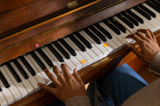 Female hands pressing upright piano keys at home, showing yellow stickers and sweater cuffs
