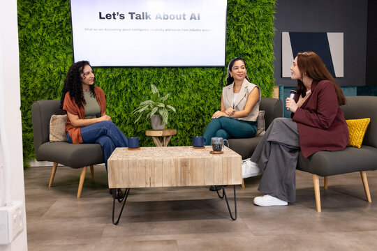 Female panelists in business attire sitting and discussing AI on set with screen and microphone