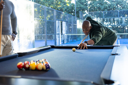 African men playing billiards, leaning over pool table with cues and racked balls in rec room
