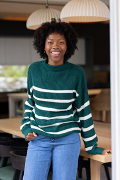 Woman leaning on large light-wood dining table in modern kitchen smiling with hoop earrings