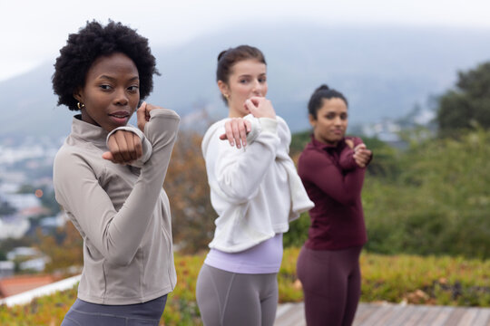 Diverse women stretching arms across chests on wooden deck in leggings with misty hills, copy space