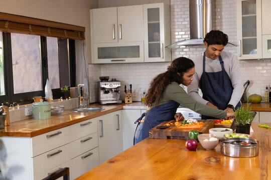 African American couple wearing aprons chopping vegetables with knife on island in kitchen at home