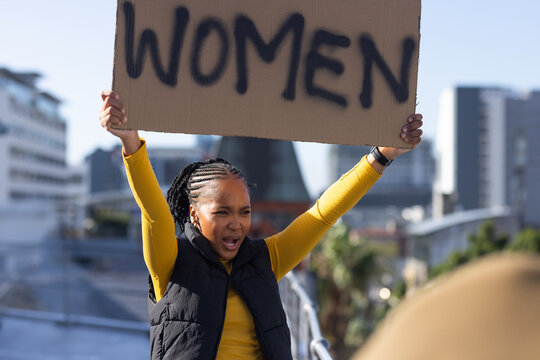 Adult woman shouting and holding cardboard sign reading WOMEN on rooftop walkway