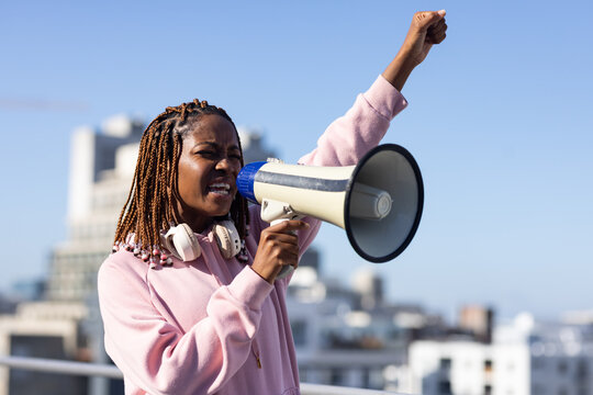 African American woman standing on roof wearing pink hoodie with megaphone and headset