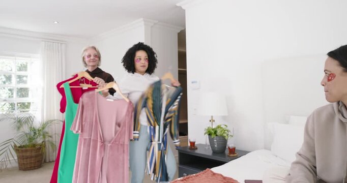 Diverse women bringing dresses, seated woman sorting jewels on bed choosing look, copy space