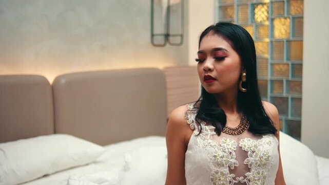 Elegant Woman in White Dress Sitting on Bed in Hotel Room