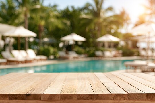Empty wooden table before blurred pool, loungers, and palm trees