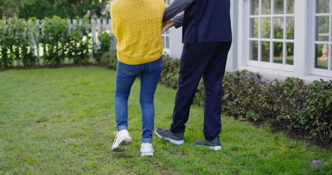Senior Chinese woman pointing, African American caregiver steadying arm for balance walking in yard