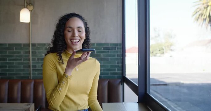 African American woman in mustard top reading message tapping phone dictating reply at cafe counter