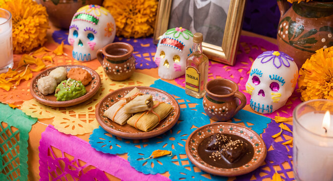 Festive Dia de los Muertos ofrenda table decorated with brightly decorated painted skulls clay dishes pan de muerto and yellow marigold petals