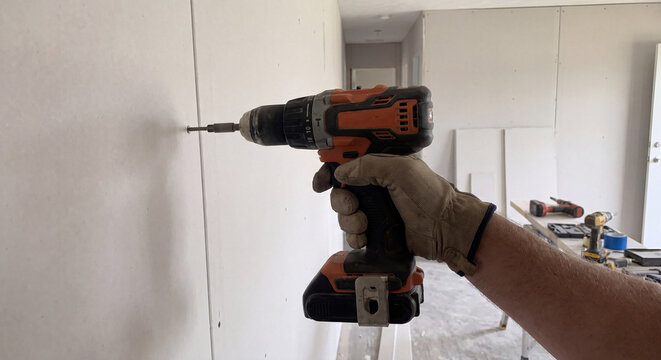 Close up view of worker hand using battery powered cordless drill driver to install fastening screw into wall structure during interior remodel