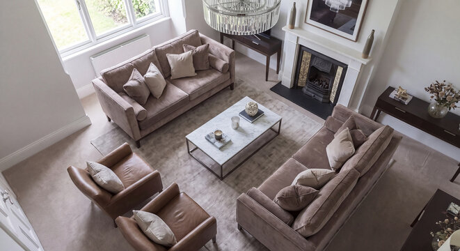 Elevated perspective of an open concept luxury living room displaying twin upholstered sofas leather armchairs fireplace and a marble coffee table on hardwood floor